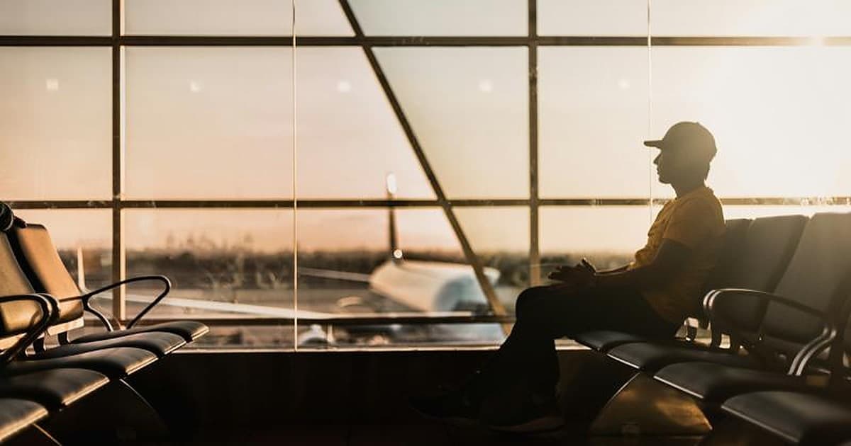 Pessoa aguardando em aeroporto diante de grandes janelas, com avião ao fundo.